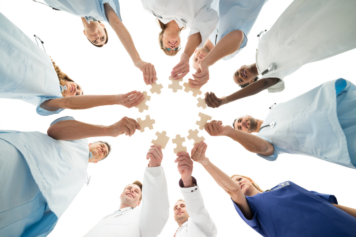 Image of a dental team joining jigsaw pieces in a huddle denoting teamwork.